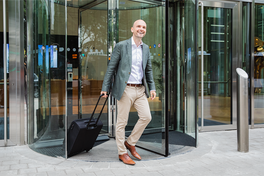 Happy man leaving a building with his suitcase. 